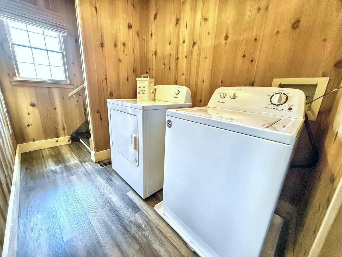 A practical yet inviting laundry area with a washer and dryer, a window letting in natural light, and warm wood paneling.
