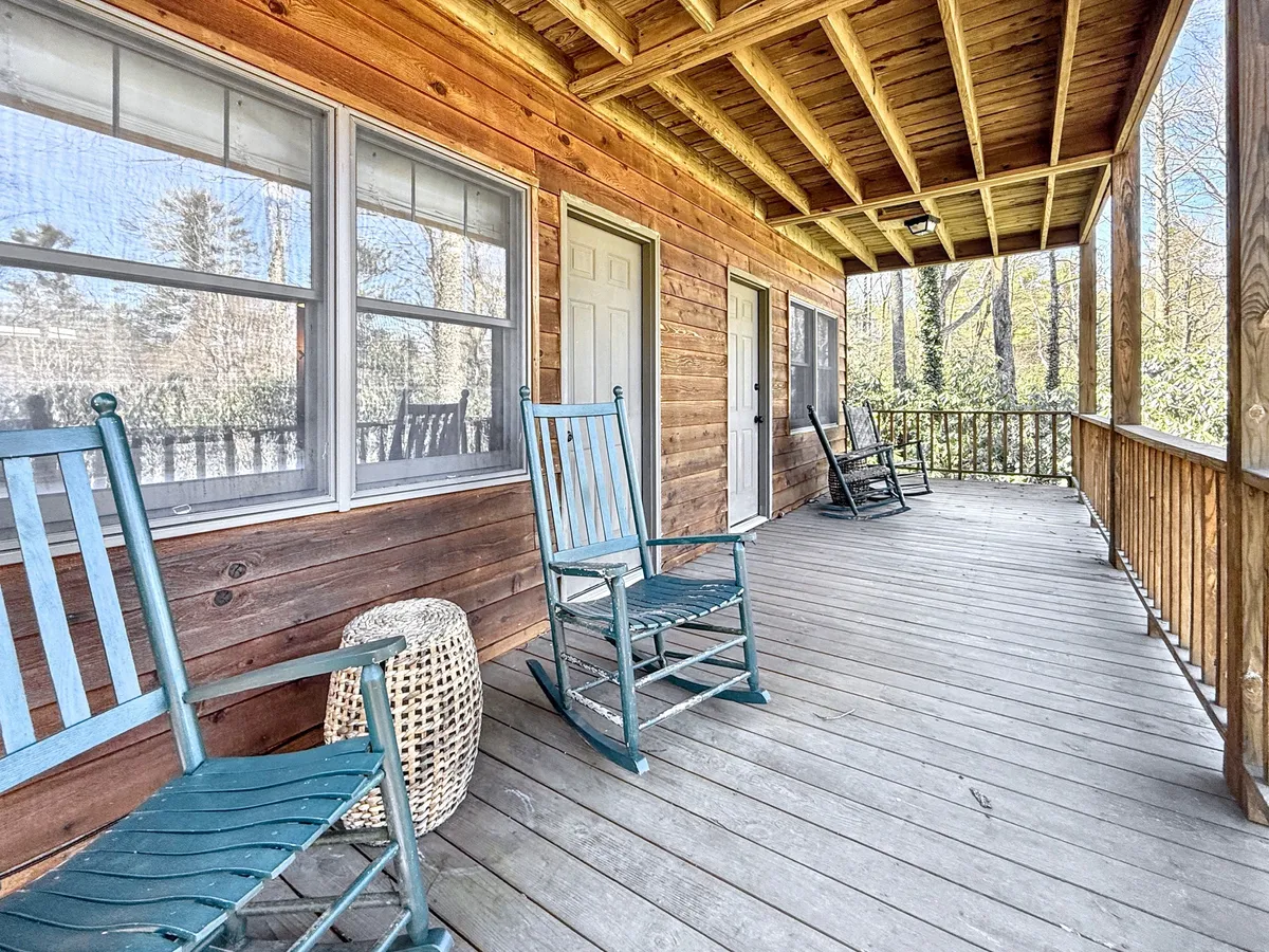 A pair of classic wooden rocking chairs sit on a deck, looking out over natural woodlands. The scene is peaceful and inviting, suggesting a perfect spot for unwinding, reading, or enjoying conversation while immersed in the sights and sounds of nature.