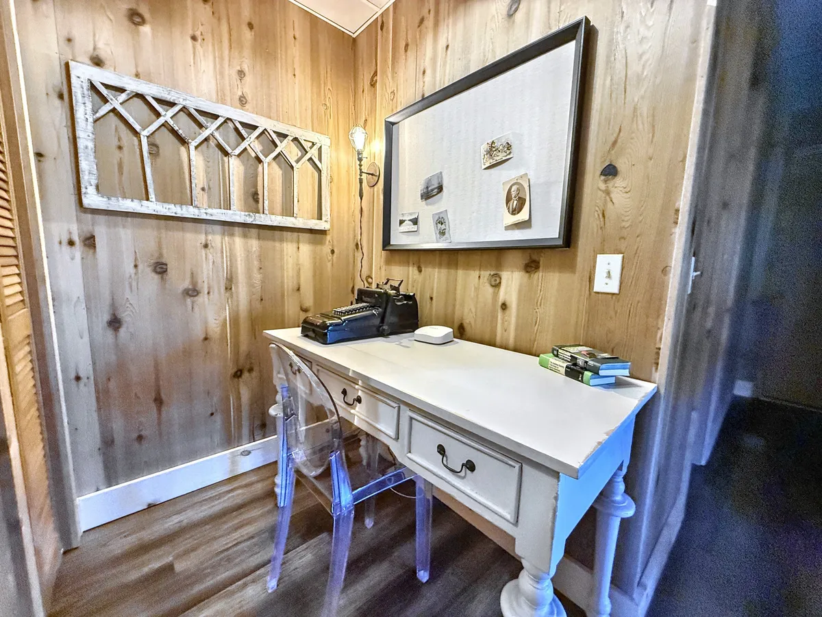 A dedicated workspace featuring a writing desk, vintage typewriter, framed photographs, and a chandelier-style light. The space evokes creativity and is positioned for productivity and comfort.