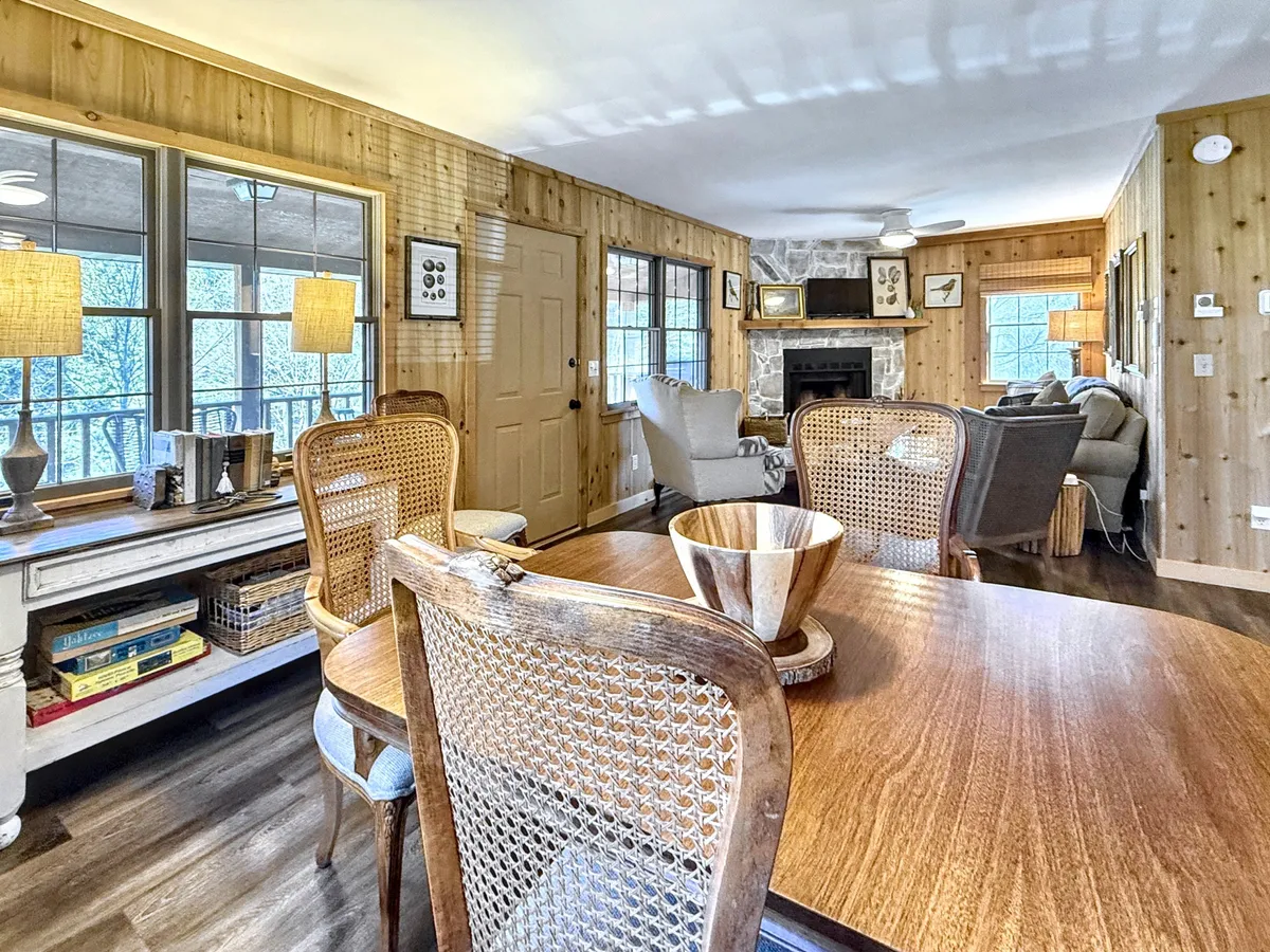 This image features a warmly lit interior with a stone fireplace, a dining table with a wooden bowl, comfortable seating, and windows that let in ample natural light. The setting exudes a sense of calm and inspires productivity, while the inviting seating area offers a place to relax after work or during breaks.