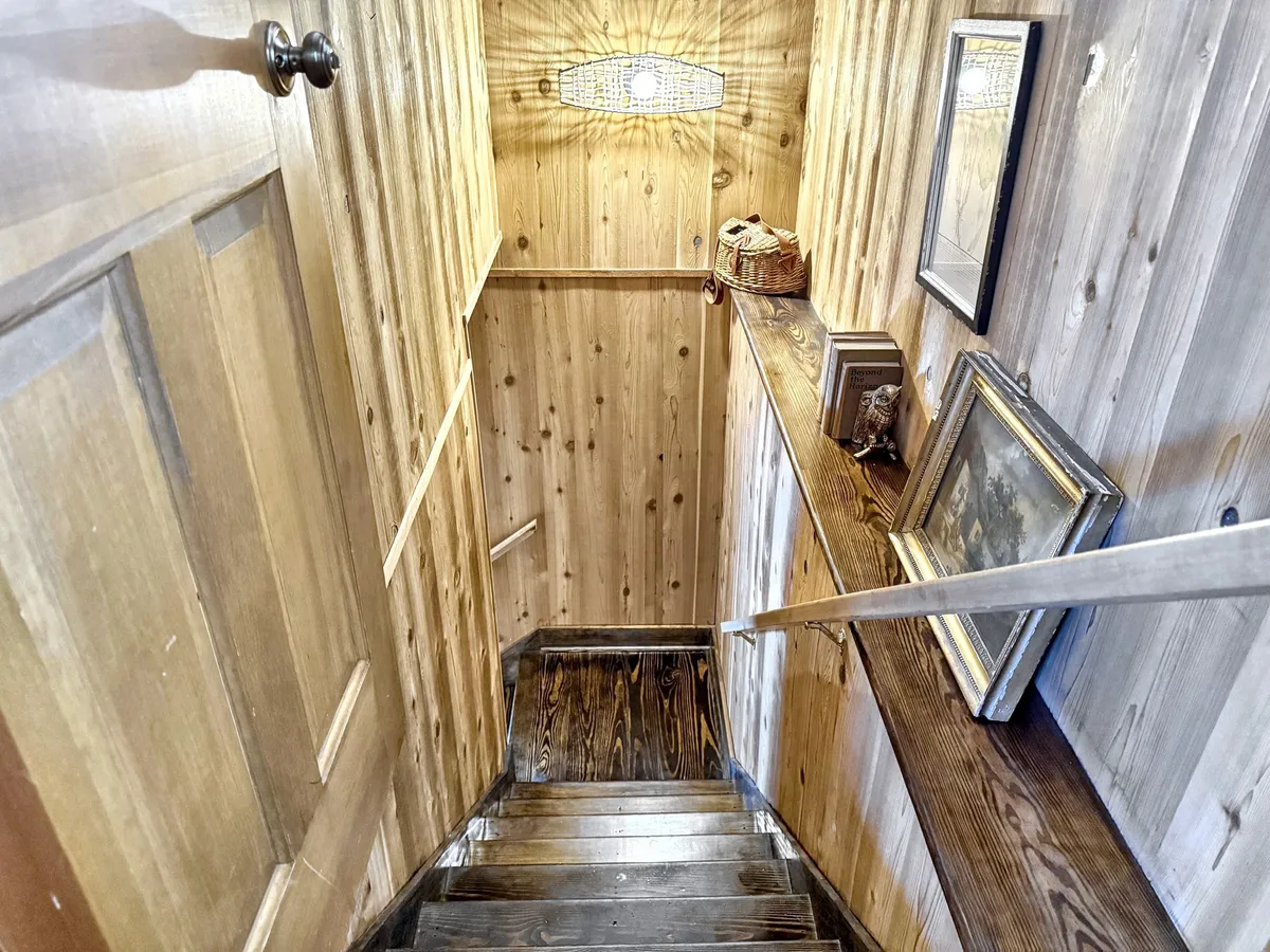 Depicting a wooden staircase with decorative items on the railing, a light fixture overhead, and a rustic wooden door, this image captures the sense of movement and transition within the home, suggesting easy access to different parts of the house and the possibility of stepping outside for breaks.