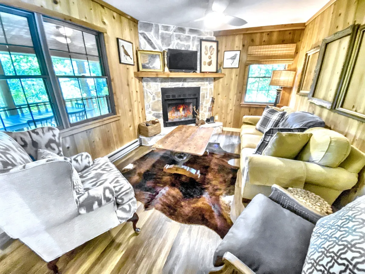 A cozy gathering space featuring a stone fireplace, comfortable seating, and rustic décor, evoking the warmth of autumn and winter in the Highlands. The inviting atmosphere is perfect for relaxing after a day spent exploring outdoors or enjoying the changing seasons through the windows.